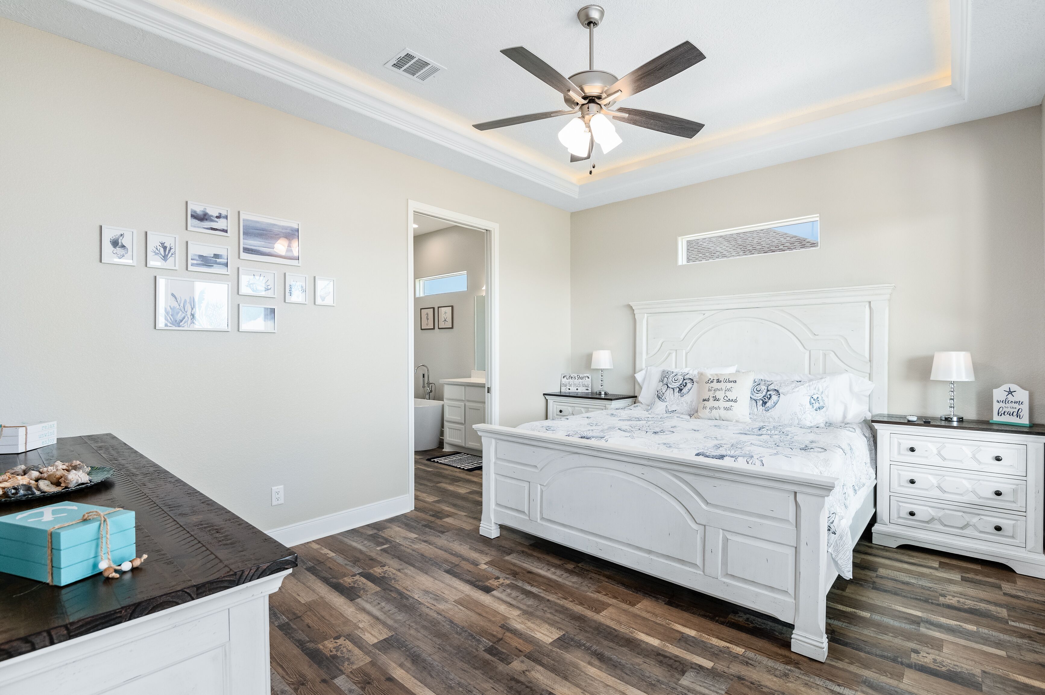 Une chambre à coucher avec un lit blanc, un ventilateur de plafond, une table de chevet et une commode.