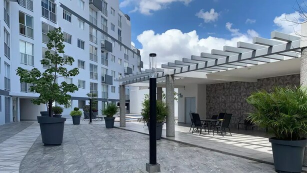 Moderni ulkotila, jossa on istutusaltaissa olevia kasveja, pergola ja ruokailuryhmä pöytineen ja tuoleineen.