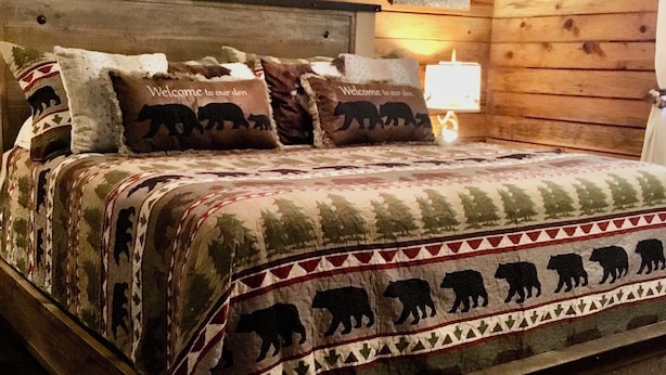 Une chambre à coucher de style cabane en bois, avec un lit, des oreillers, un ventilateur de plafond et une table de chevet avec une lampe.