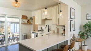 A modern kitchen with white cabinets, a large island, pendant lights, and a dining area with chairs.