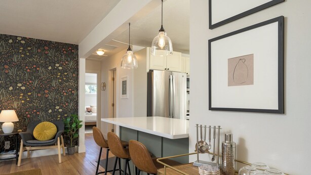 A modern kitchen with a central island, bar stools, pendant lighting, and a refrigerator.