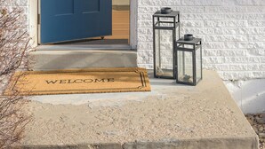 A front door with a dark blue door, a welcome mat, and two lanterns on the porch.