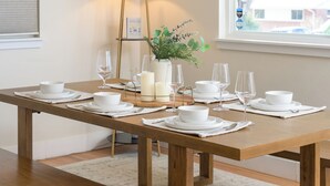 A dining table set with white plates, bowls, and glasses, a vase with greenery, and candles.