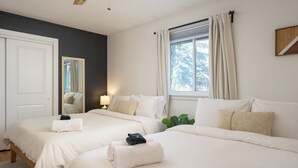 A hotel room with two beds, a large mirror, a window with curtains, and a plant.