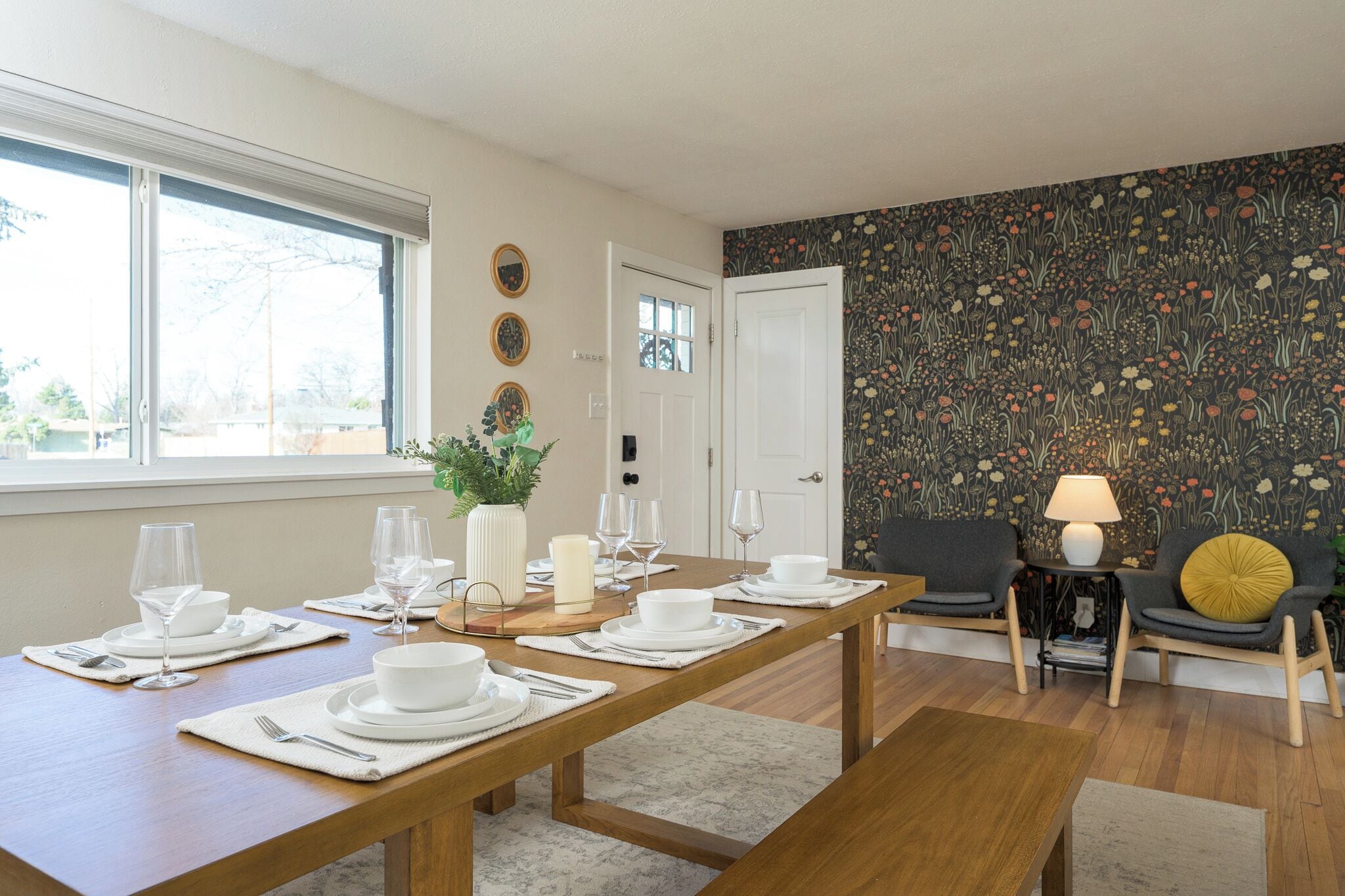 A dining area with a wooden table set for four, a sofa, and a patterned wall.