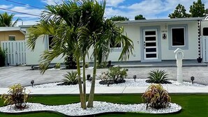 A modern building with a white facade, a gated entrance, and a well-maintained lawn with palm trees and shrubs. - Elegant beautiful house w/pool 10 min from Miami Int. Airport (Hialeah)