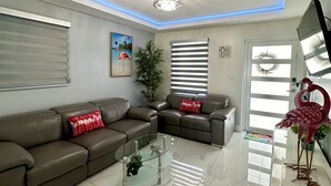A modern living room with a sectional sofa, a glass coffee table, a potted plant, and a decorative flamingo. - Elegant beautiful house w/pool 10 min from Miami Int. Airport (Hialeah)