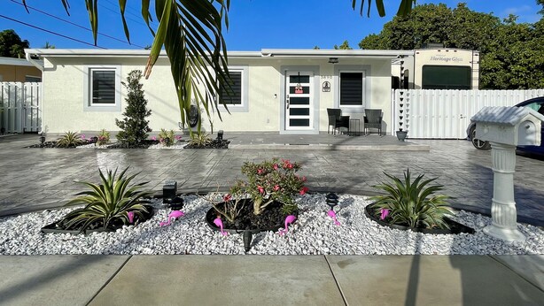 A modern single-story house with a white exterior, a covered patio area, and a small garden with decorative flamingos. - Elegant beautiful house w/pool 10 min from Miami Int. Airport (Hialeah)