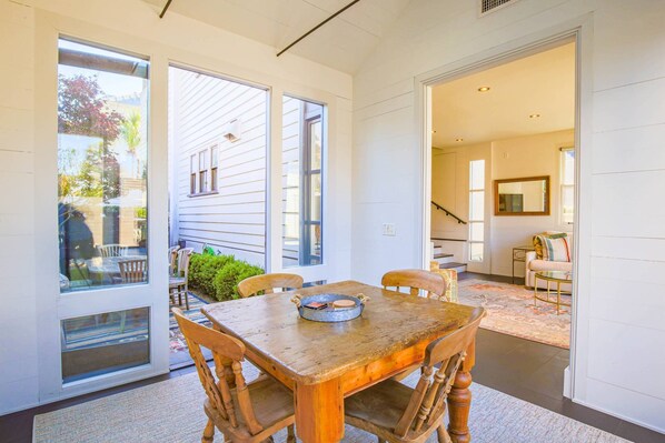 A dining area with a wooden table and chairs, large windows, and a view of the outside.