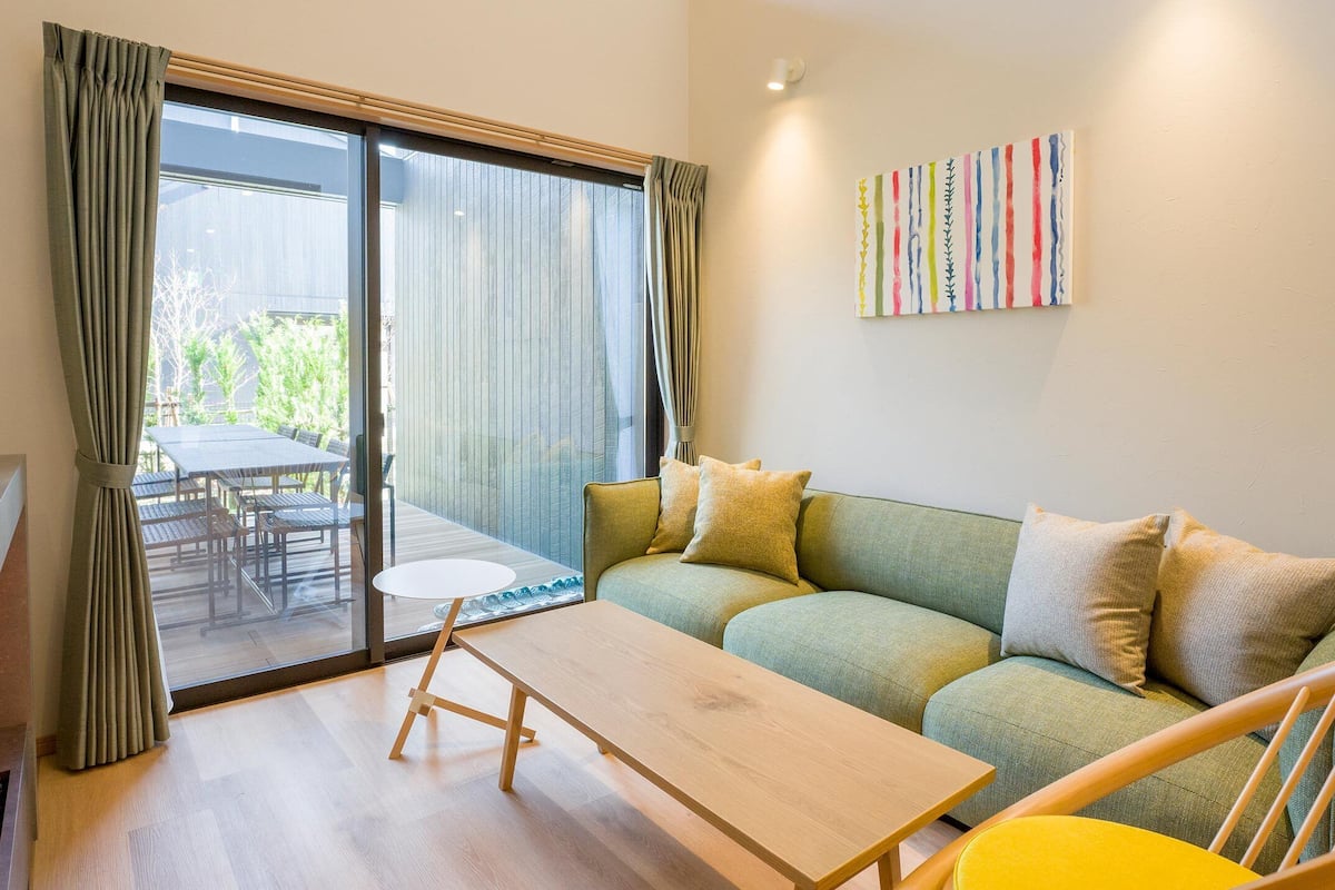 A modern living room with a sofa, a small table, and a sliding glass door leading to an outdoor patio.