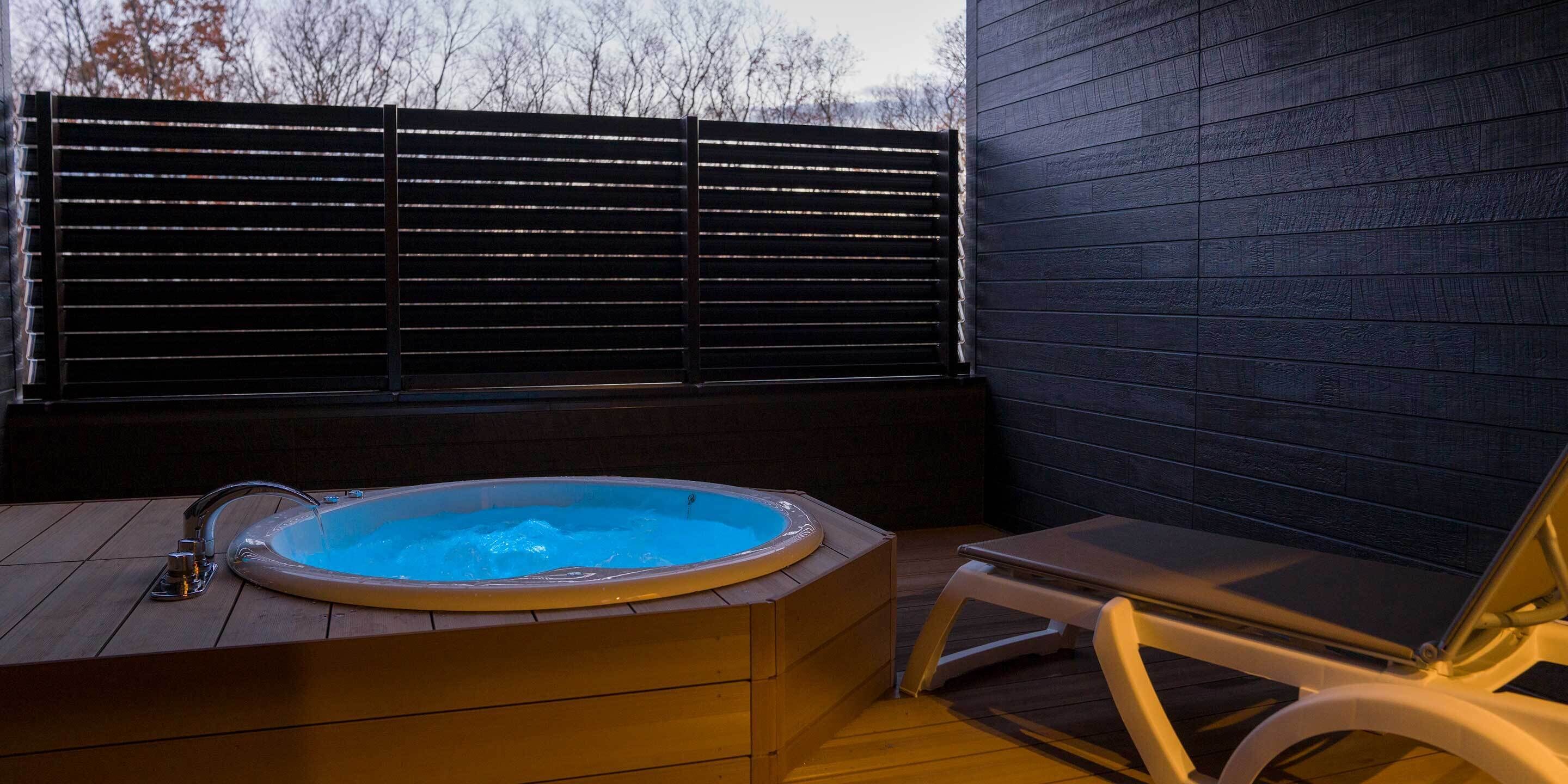 A hot tub with a wooden deck and a lounge chair.