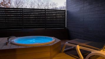 A hot tub with a wooden deck and a lounge chair.