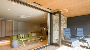A modern living room with a green sofa, a small round table, and a glass door leading to an outdoor area with blue chairs. - Rakuten STAY VILLA Nasu (Nasu)