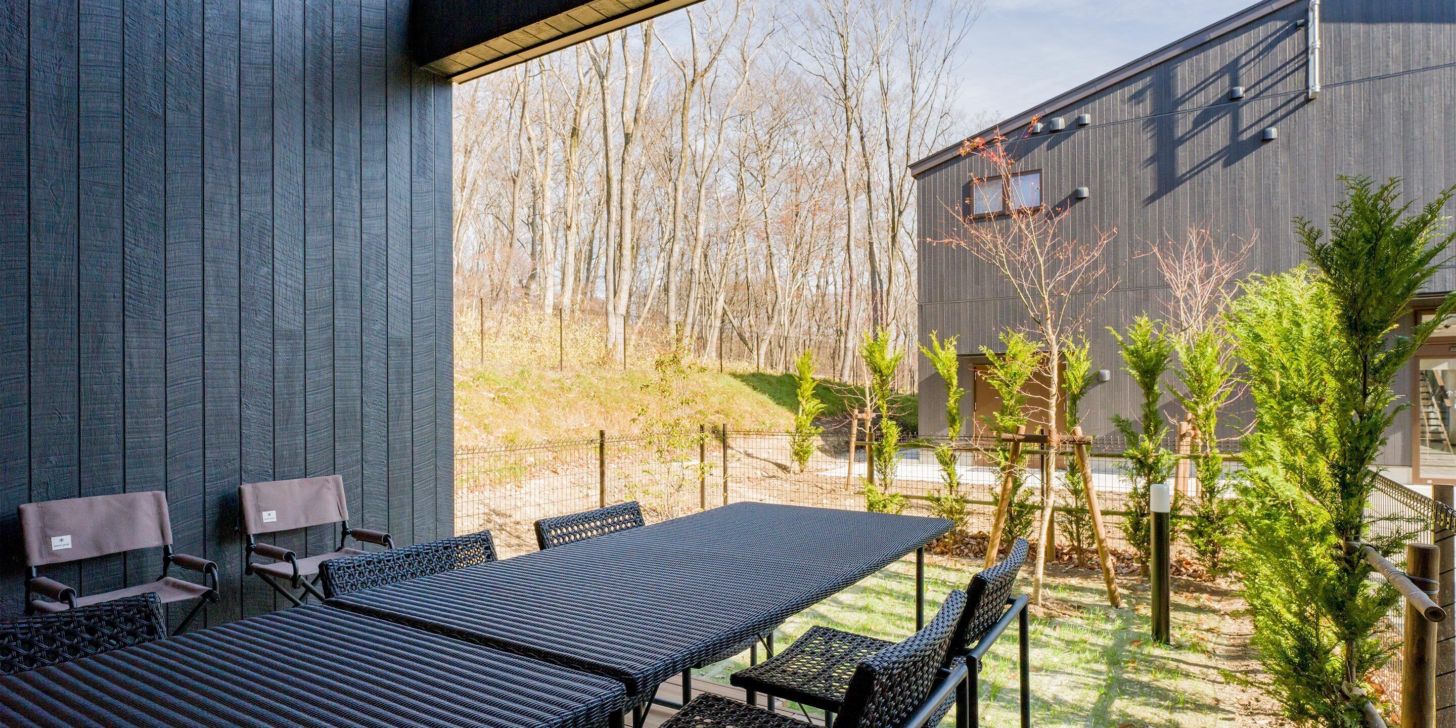 Eine Terrasse im Freien mit Tisch und Stühlen, umgeben von einem Holzzaun und Bäumen.