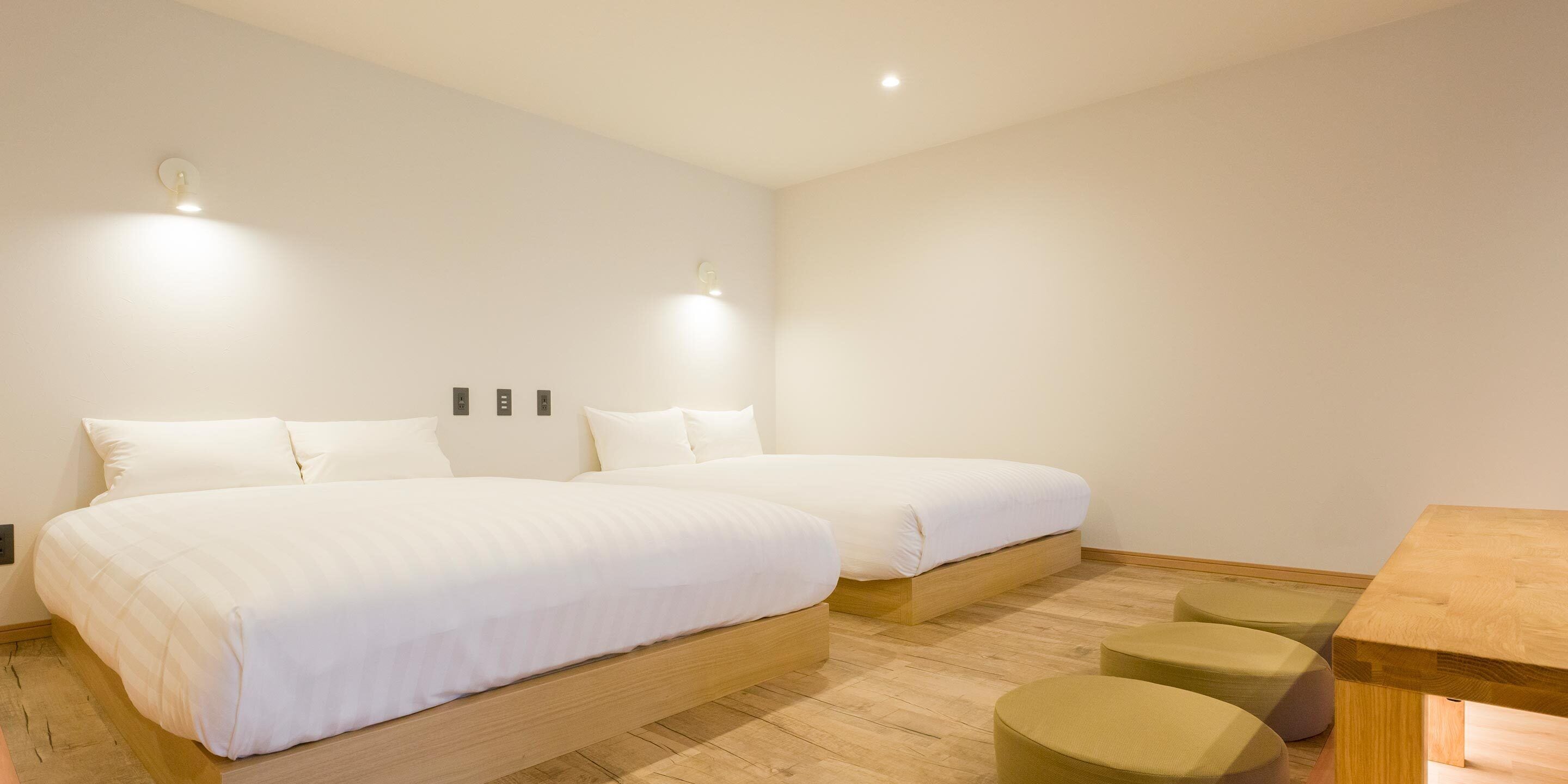 Une chambre d’hôtel moderne avec deux lits, une table en bois et un petit coin salon.