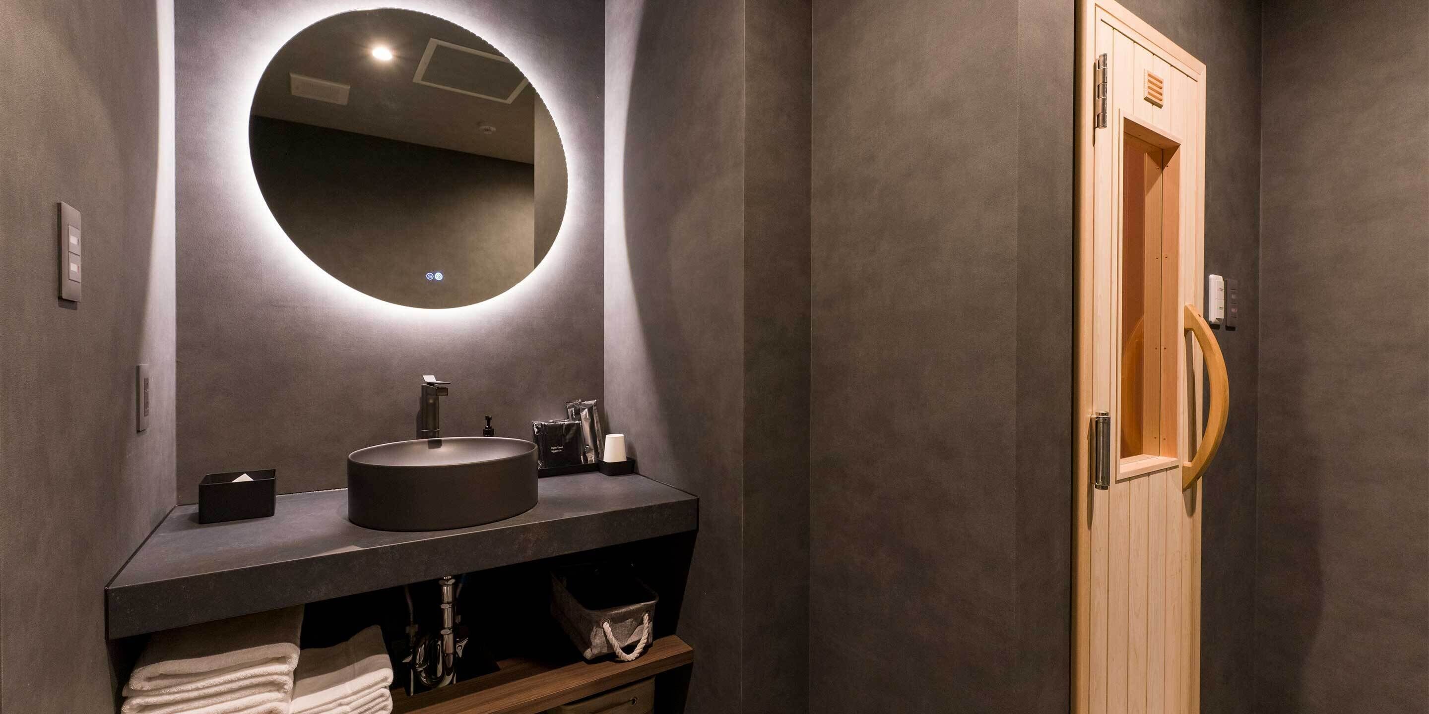 A modern bathroom with a round mirror, dark countertop, and a wooden door.
