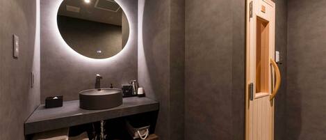 A modern bathroom with a round mirror, dark countertop, and a wooden door.