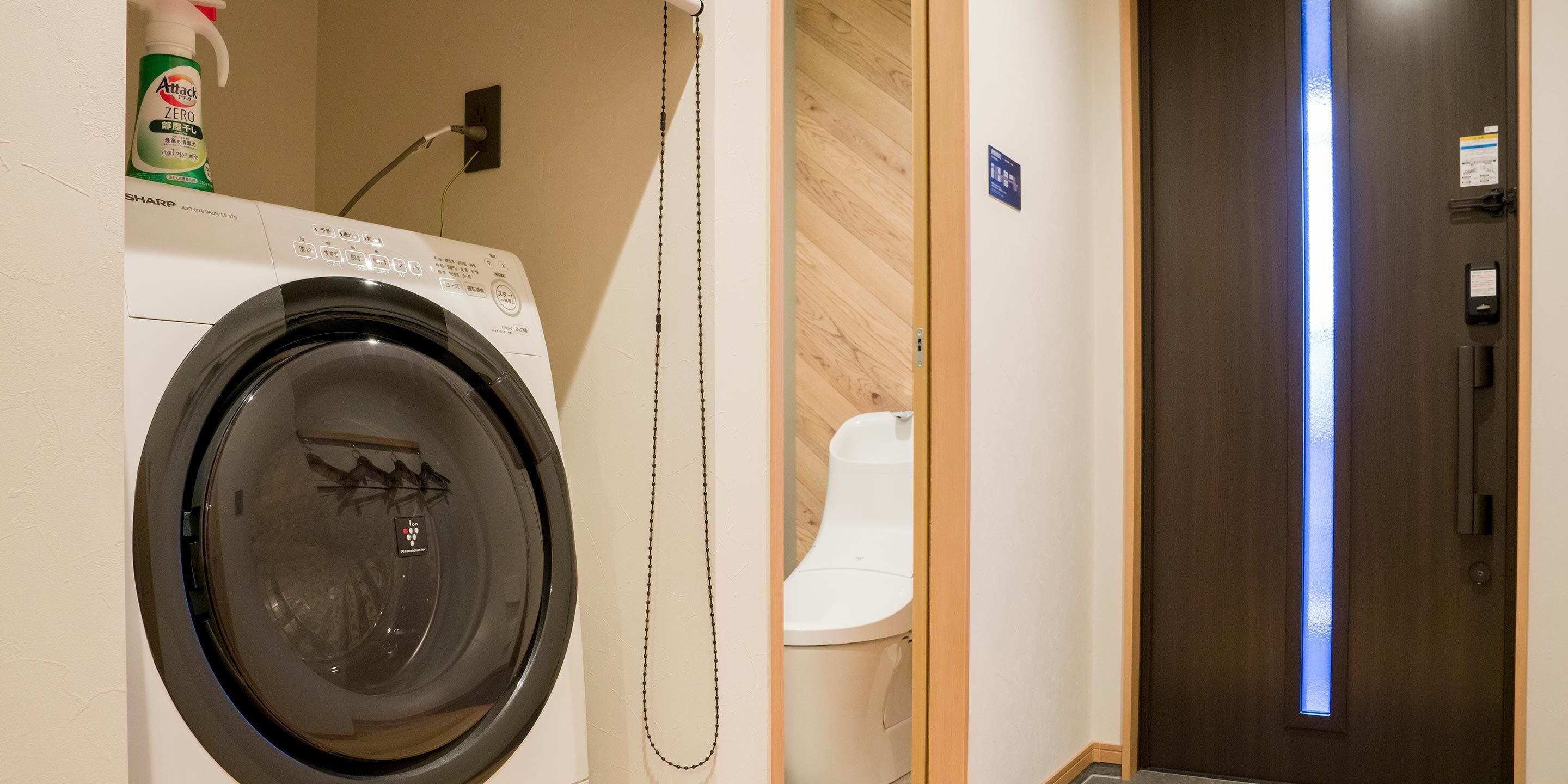 A compact hotel room with a washing machine, a toilet, and a wooden door.