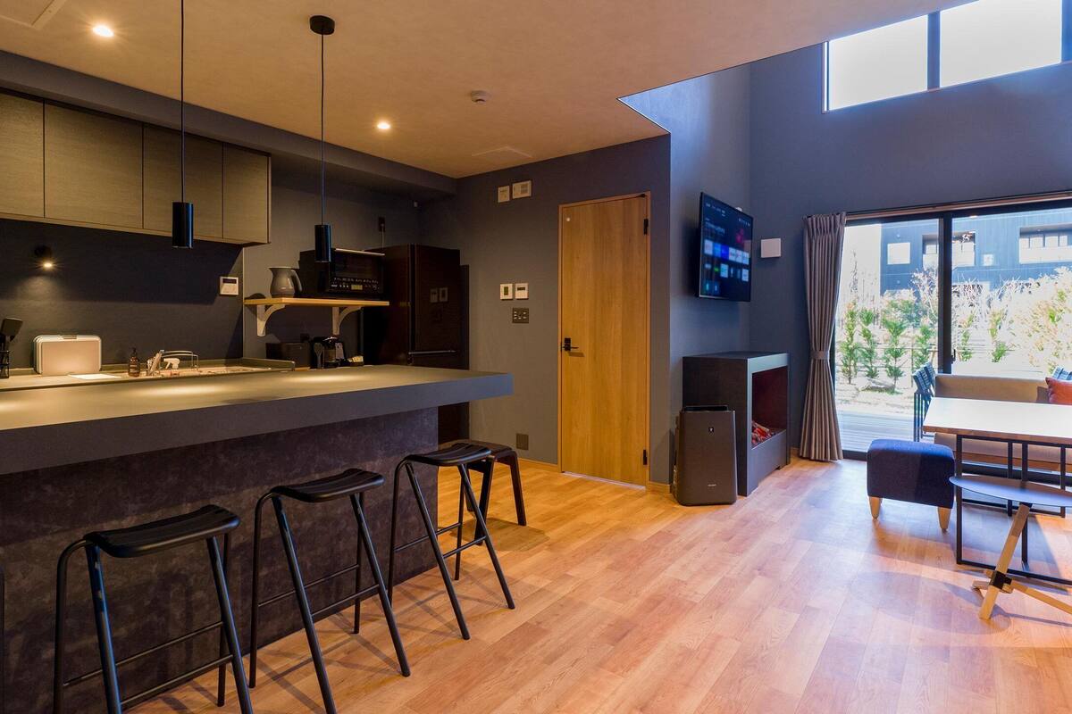 A modern kitchen with a bar area, wooden flooring, and a TV mounted on the wall.