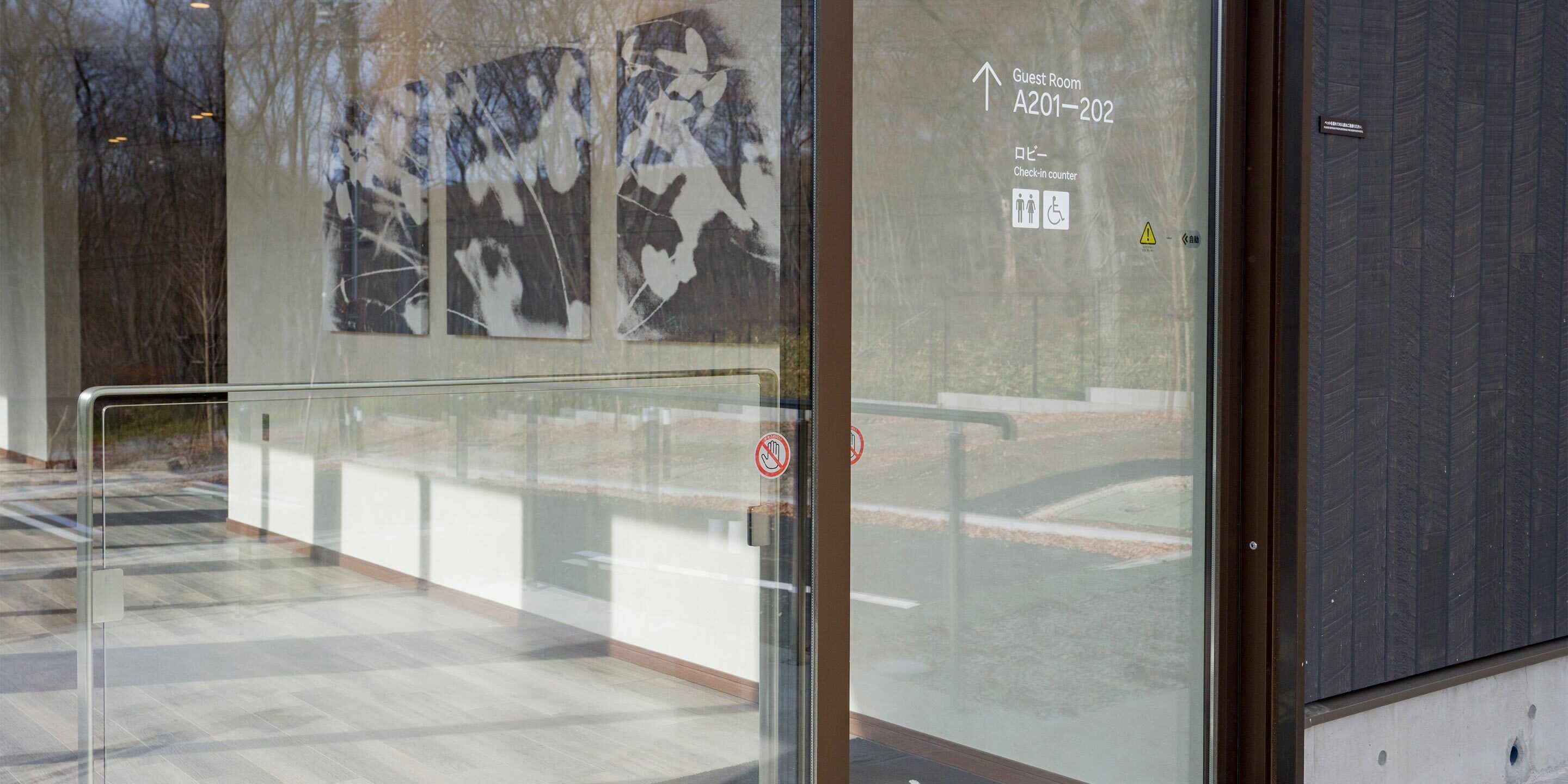 Une porte vitrée avec une enseigne indiquant le comptoir d’enregistrement, une autre interdisant de fumer, et une flèche indiquant la direction des chambres A201 et A202.