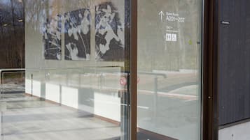 Una puerta de cristal con un cartel de recepción, un letrero de prohibido fumar y una flecha indicando las habitaciones de huéspedes A201-202.
