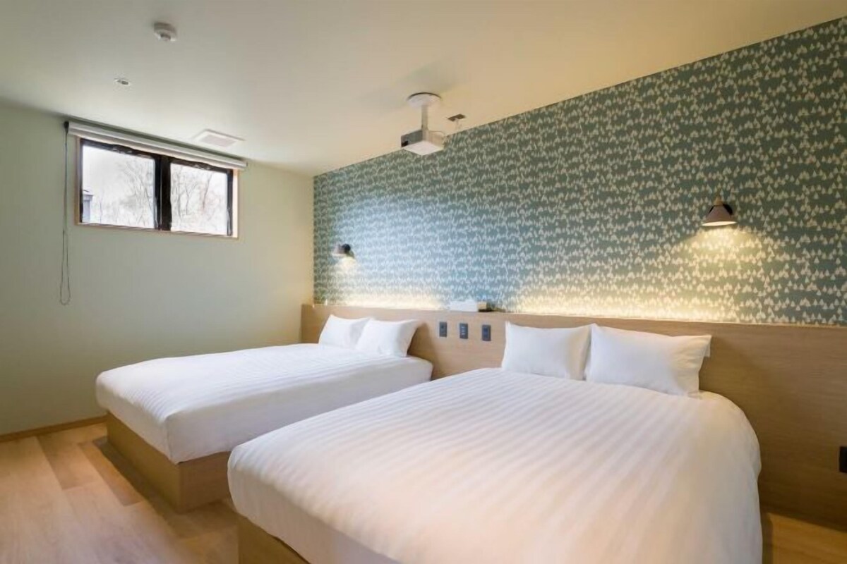 A hotel room with two single beds, a window, a patterned wall, and a ceiling fan.