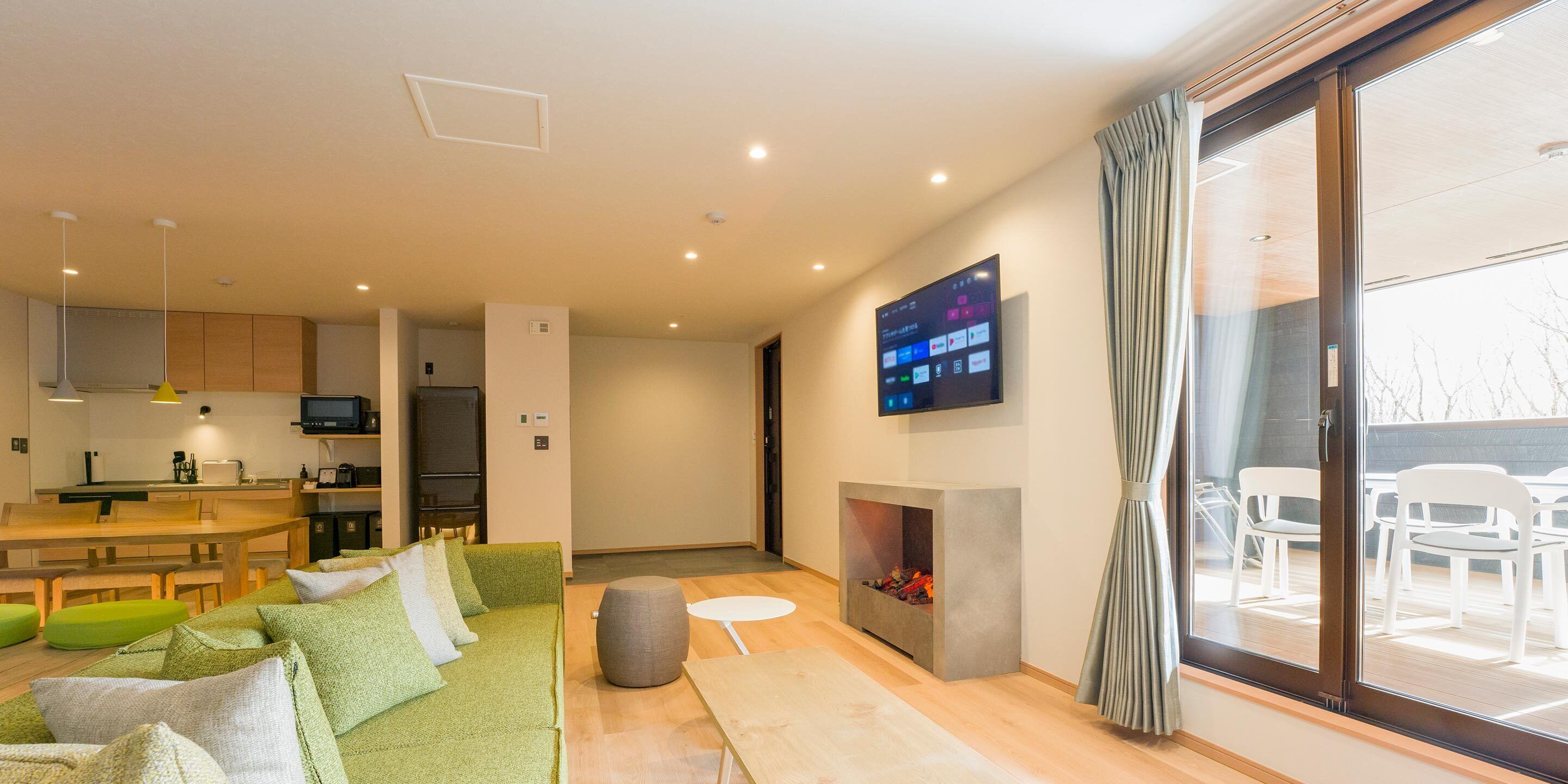 Un salon moderne avec un canapé vert, une cheminée et un téléviseur fixé au mur.