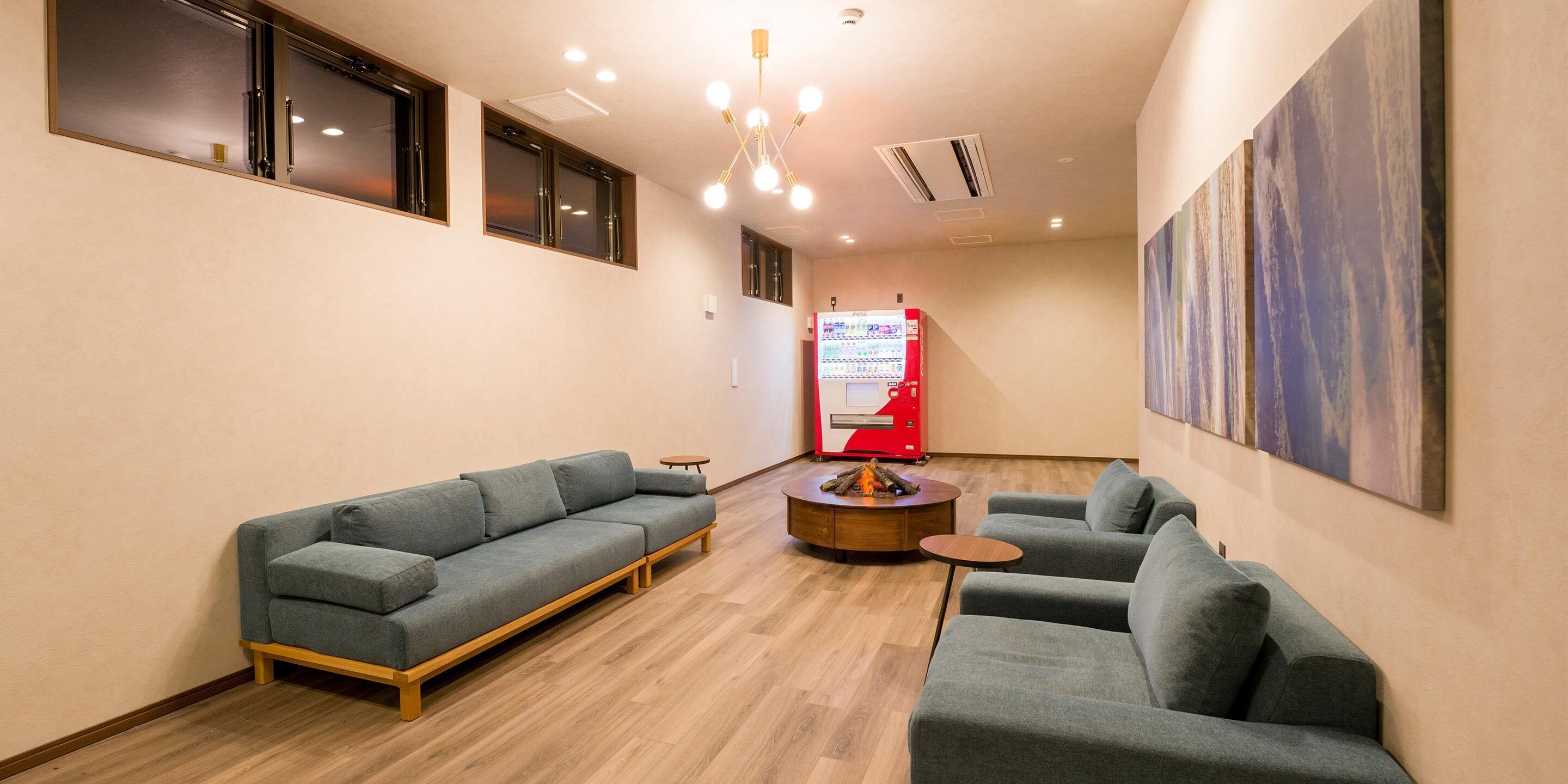 Un interior moderno con dos sofás grises, una pequeña mesa de centro de madera y una máquina expendedora roja.