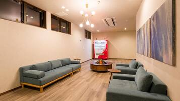 Un interior moderno con dos sofás grises, una pequeña mesa de centro de madera y una máquina expendedora roja.