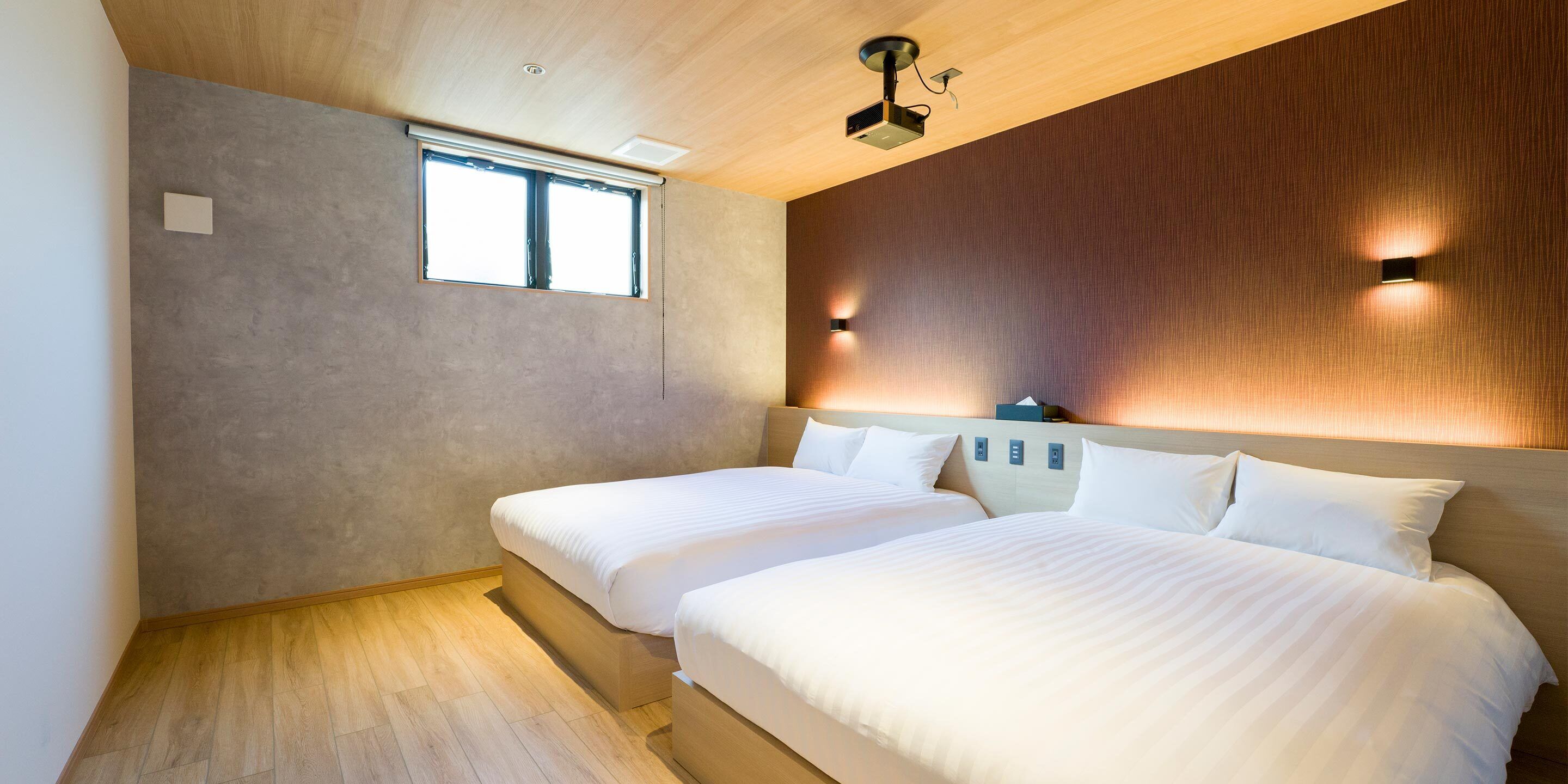 A modern hotel room with two beds, a large window, and a wooden ceiling.