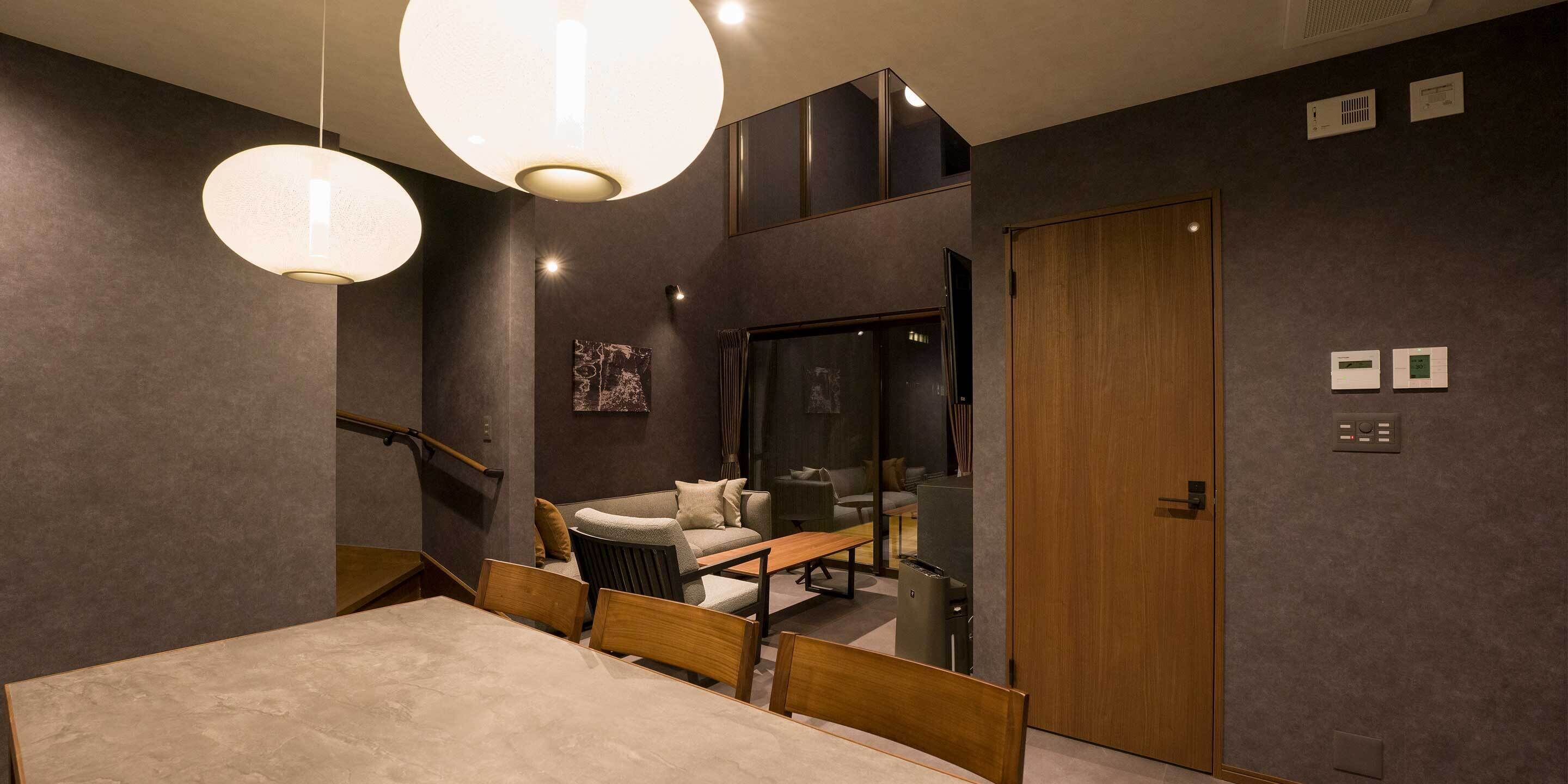 Un comedor moderno con una mesa y sillas de madera, un sofá y dos lámparas colgantes.
