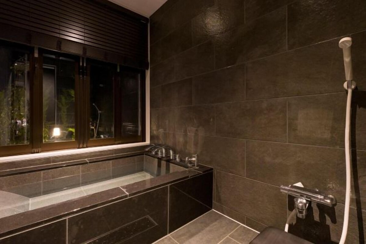 A modern bathroom with a large bathtub, a shower area, and a window with blinds.