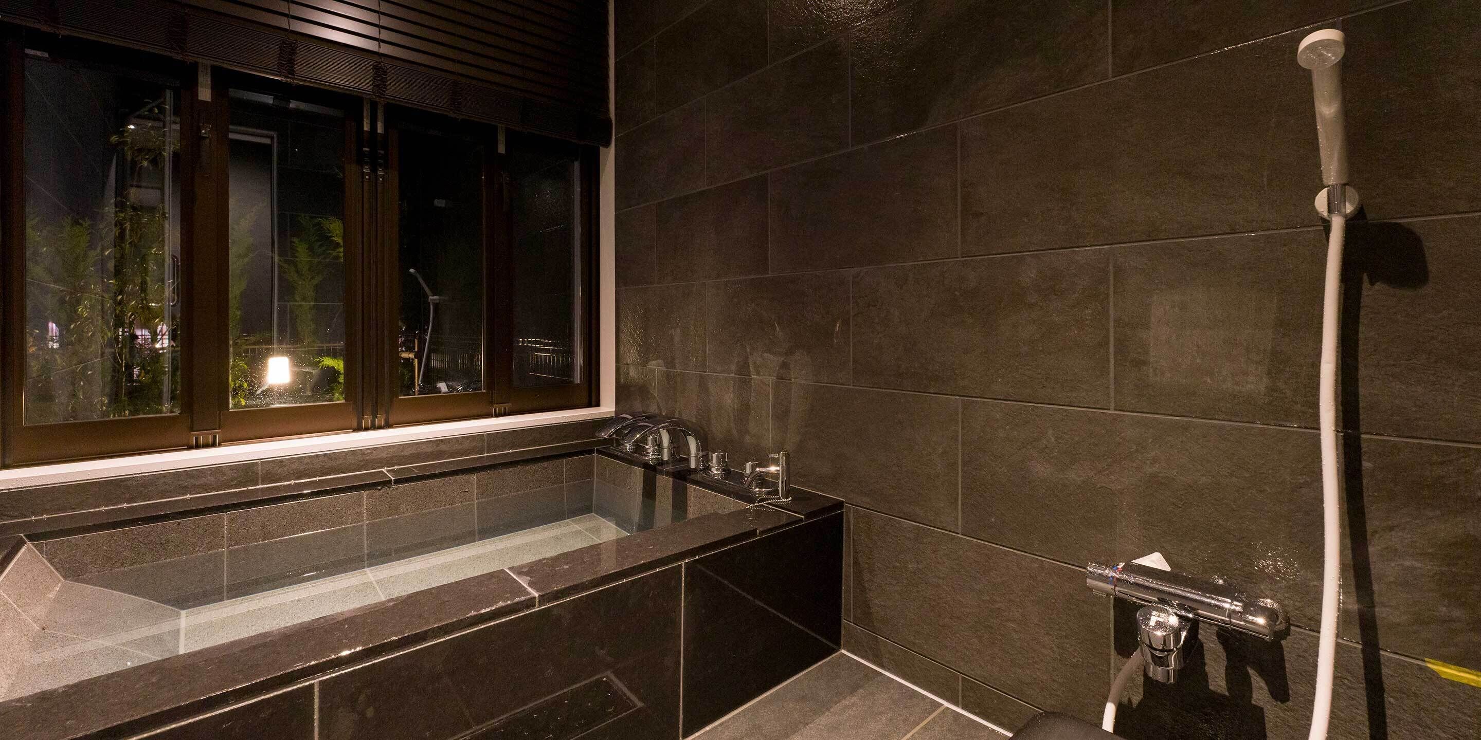 A modern bathroom with a glass-enclosed bathtub, a shower, and a window overlooking a garden.