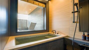 A modern bathroom with a large bathtub, a window, and a shower area.