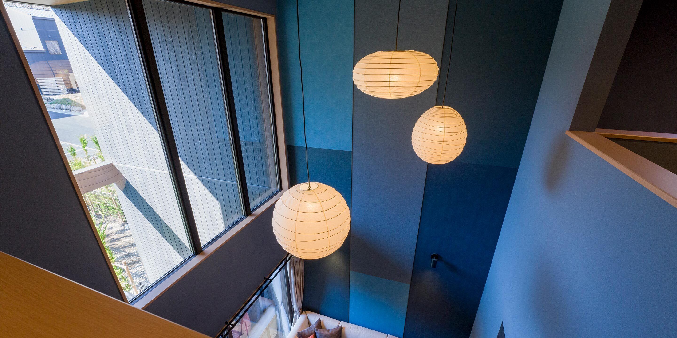A modern interior with large windows, a staircase, and hanging paper lanterns.