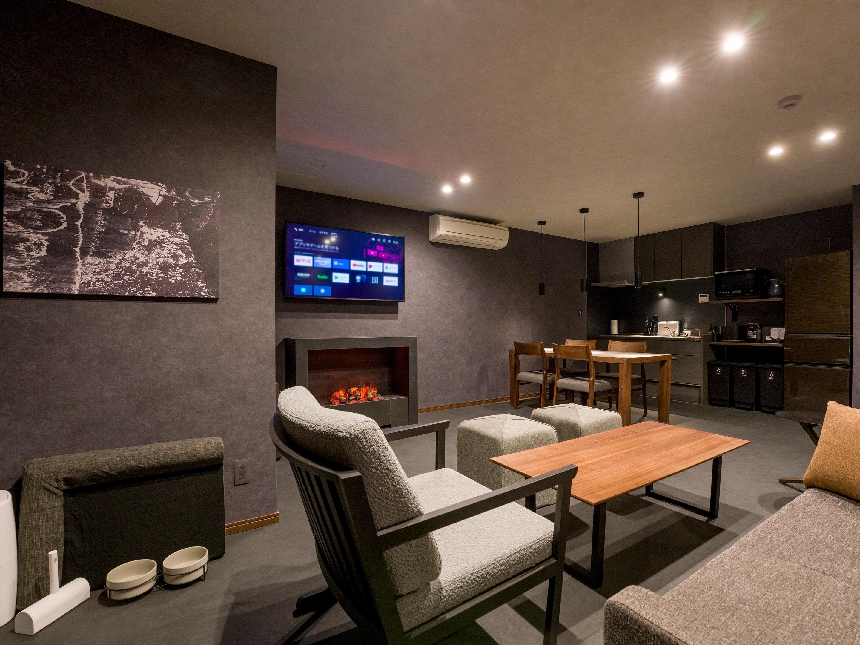 A modern living room with a fireplace, comfortable seating, a flat-screen TV, and a kitchen area.