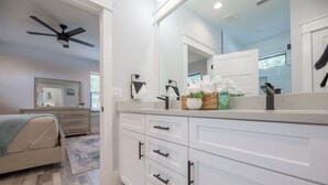 A modern bathroom with a large mirror, white cabinetry, and a ceiling fan.