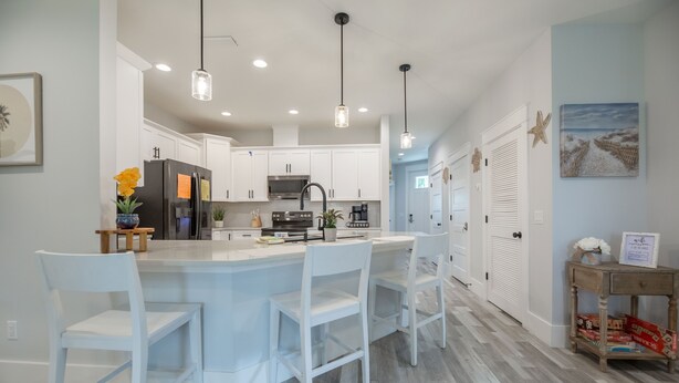 A modern kitchen with white cabinetry, a central island with bar stools, pendant lighting, and a view into the adjacent dining area.