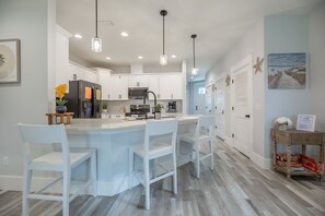 Uma cozinha moderna com armários brancos, uma ilha central com banquetas, iluminação pendente e vista para a área de jantar adjacente.