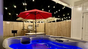 A hot tub with blue lighting, a red umbrella, and a wooden deck with string lights.