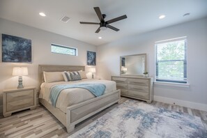 Quarto com cama, mesas de cabeceira, cômoda, ventilador de teto e janela com persianas.