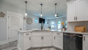 A modern kitchen with white cabinetry, a built-in dishwasher, pendant lighting, and a large island with a sink.