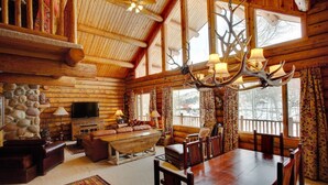 L’intérieur d’une cabane en rondins, avec un mur en pierre, des meubles en bois, un grand lustre et un téléviseur.