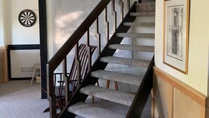 Eine Treppe mit dunkler Holzhandläufe und Teppichstufen, die zu einer Zwischenebene führt, auf der sich ein gerahmtes Bild und ein kleiner Tisch mit einem Fahrrad befinden.