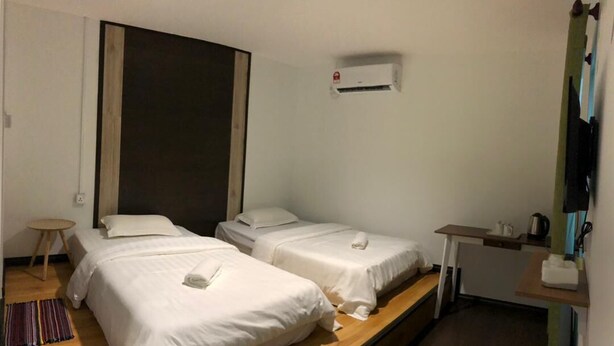 A hotel room with two single beds, a small table, a chair, an air conditioning unit, and a kitchenette. - OYO HOME 90667 Chen Room Bs (Semporna)