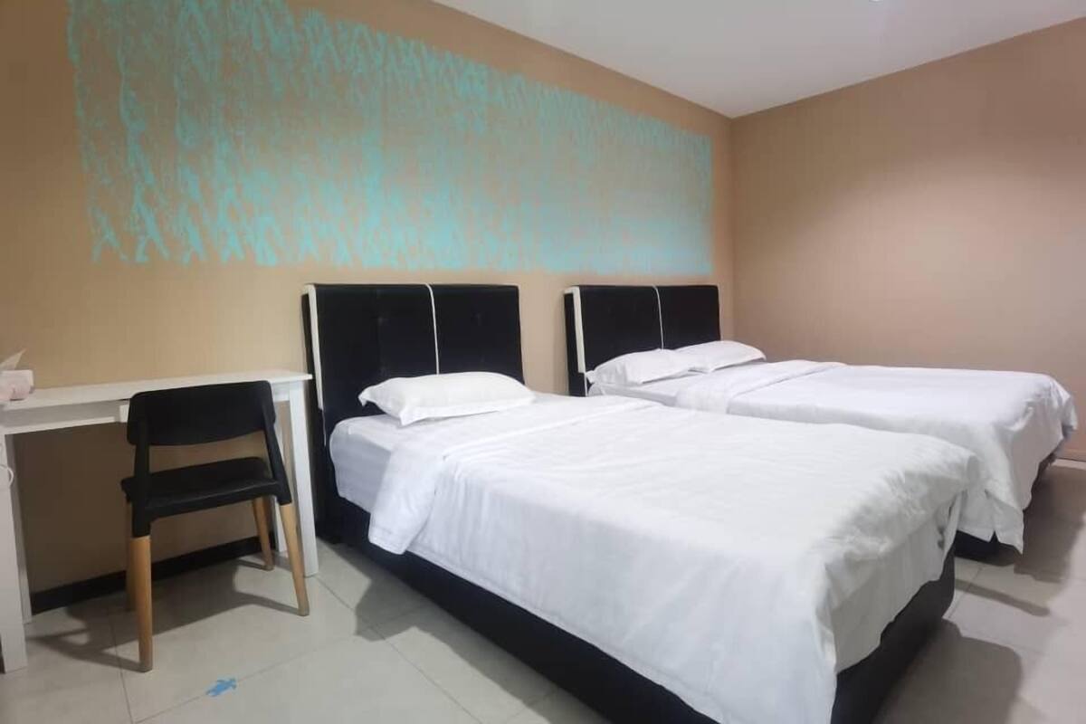 Une chambre d’hôtel avec deux lits simples, un bureau avec une chaise et une grande fresque murale abstraite.