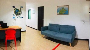 A room with a desk, a red chair, a blue sofa, and a door. - OYO HOME 90667 Chen Room Bs (Semporna)