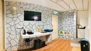 A bathroom with a stone-patterned wall, a sink with a mirror, a towel rack, and a door labeled "KELLDON". - OYO HOME 90667 Chen Room Bs (Semporna)
