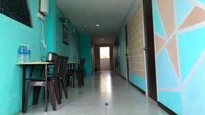 A hallway with teal walls, a tiled floor, and a table with chairs. There is a water dispenser and a power outlet on the wall. - OYO HOME 90667 Chen Room Bs (Semporna)