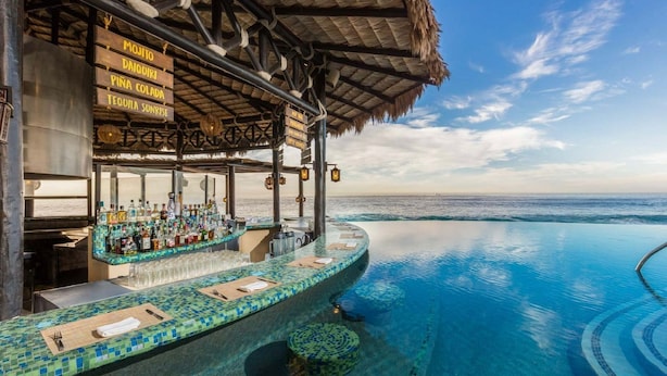 Ein Infinity-Pool mit Barbereich im tropischen Stil, inklusive eines Reetdachs und einer Schautafel mit Getränkeangeboten.
